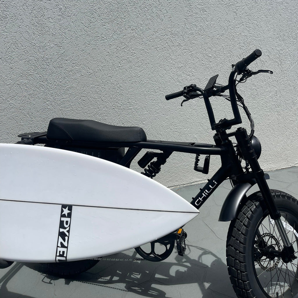 Black electric bike with a white surfboard attached against a gray wall